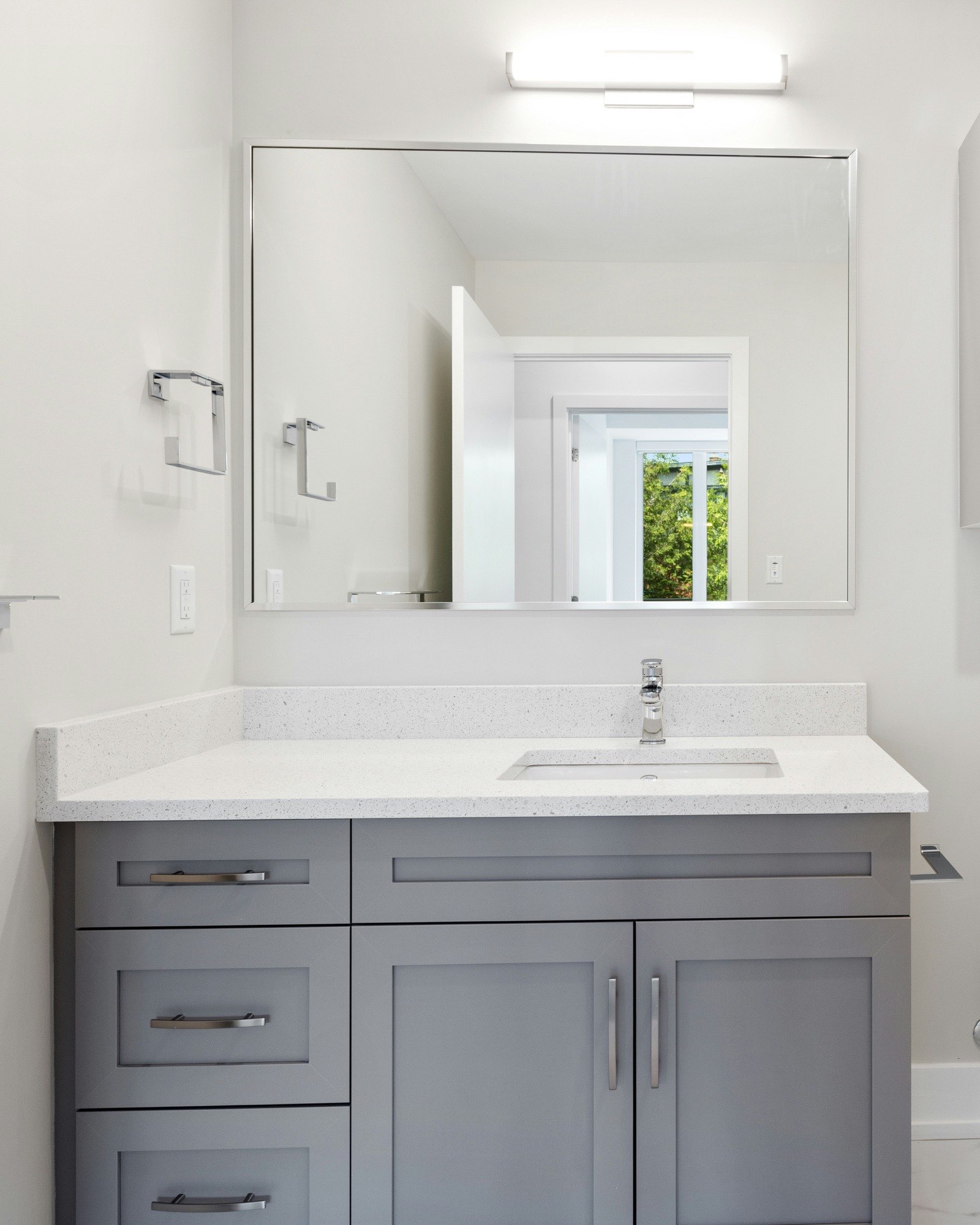 Bathroom with a grey shaker vanity, white quartz counter, wide frameless mirror, and a subway-tile tub surround