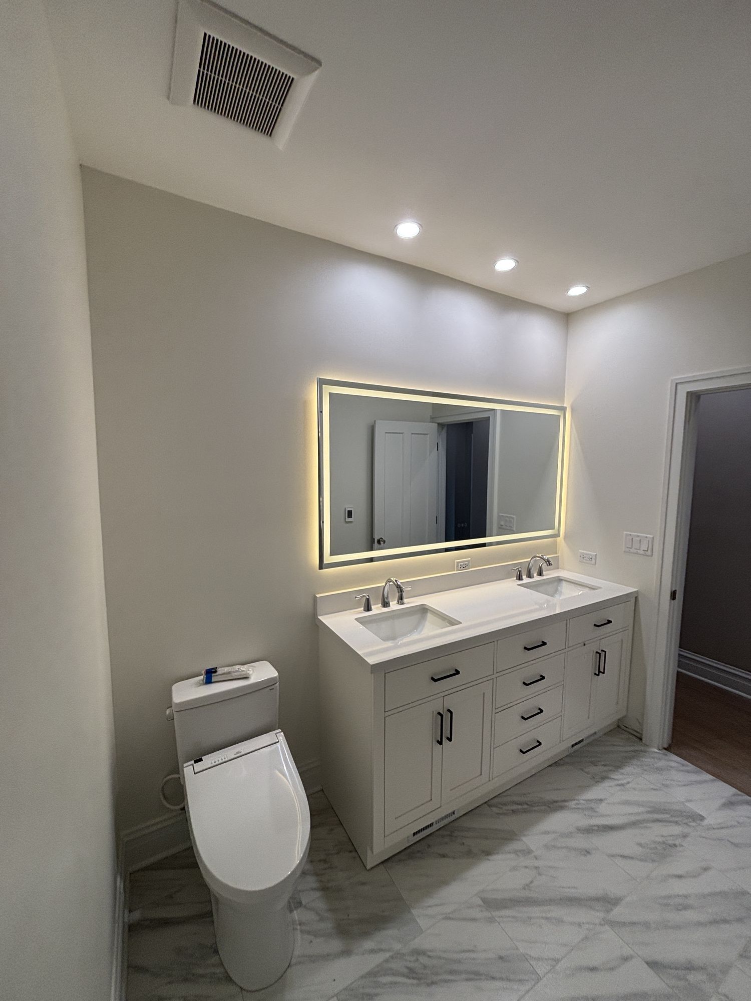 Bright bathroom with a white double vanity, backlit mirror, marble tile floor, and a smart toilet