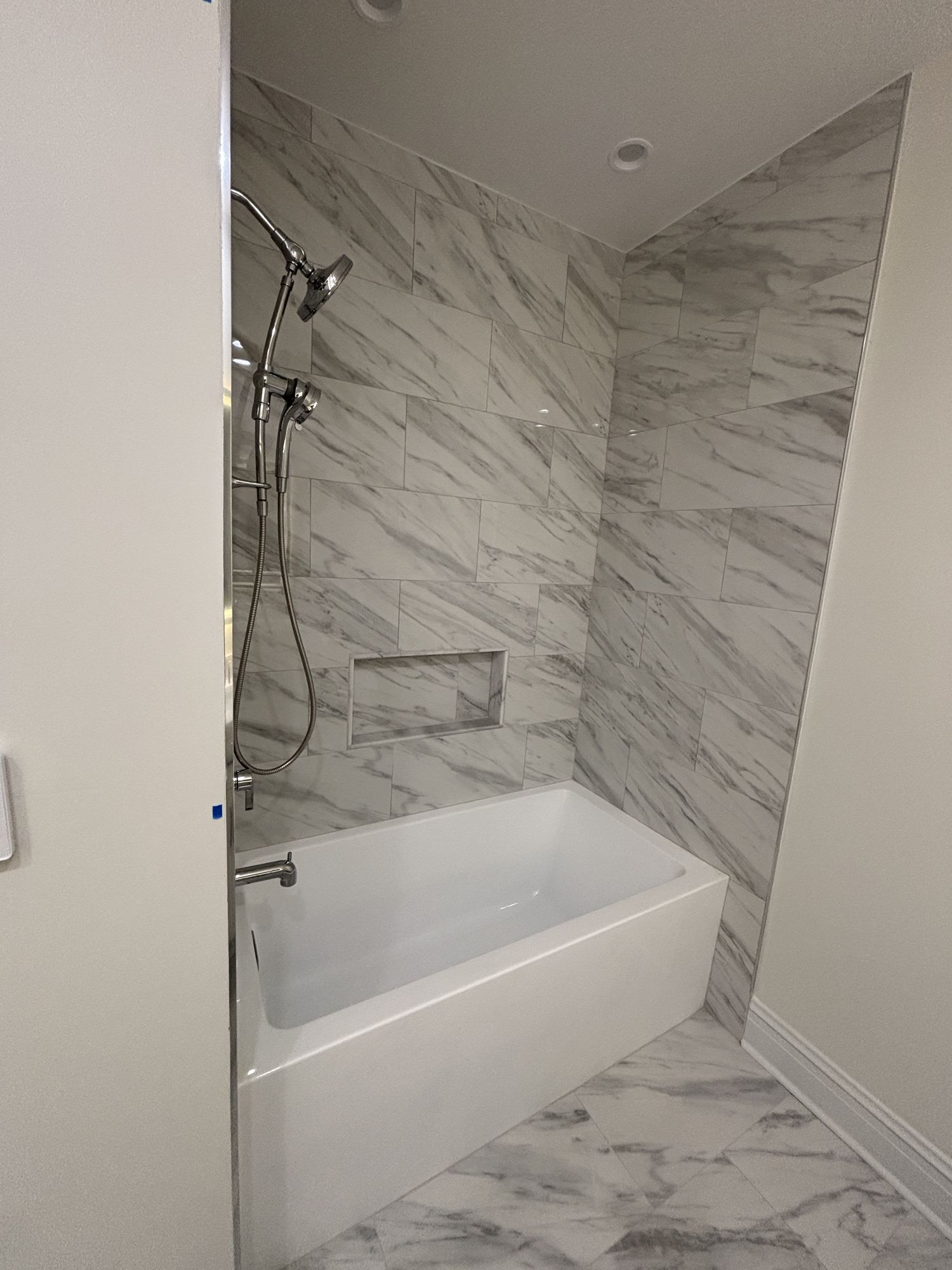 Soaking tub set into an alcove of Carrara-look marble tile with a niche
