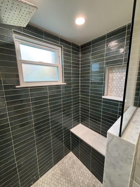 Walk-in shower wrapped in glazed green tile with a marble bench and a window