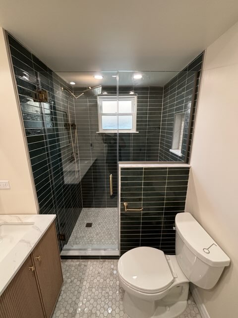 Glass-enclosed green tile shower beside the toilet and vanity