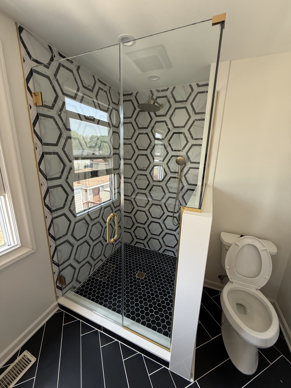 Glass shower with hexagon marble walls, brass hardware, and black herringbone floor