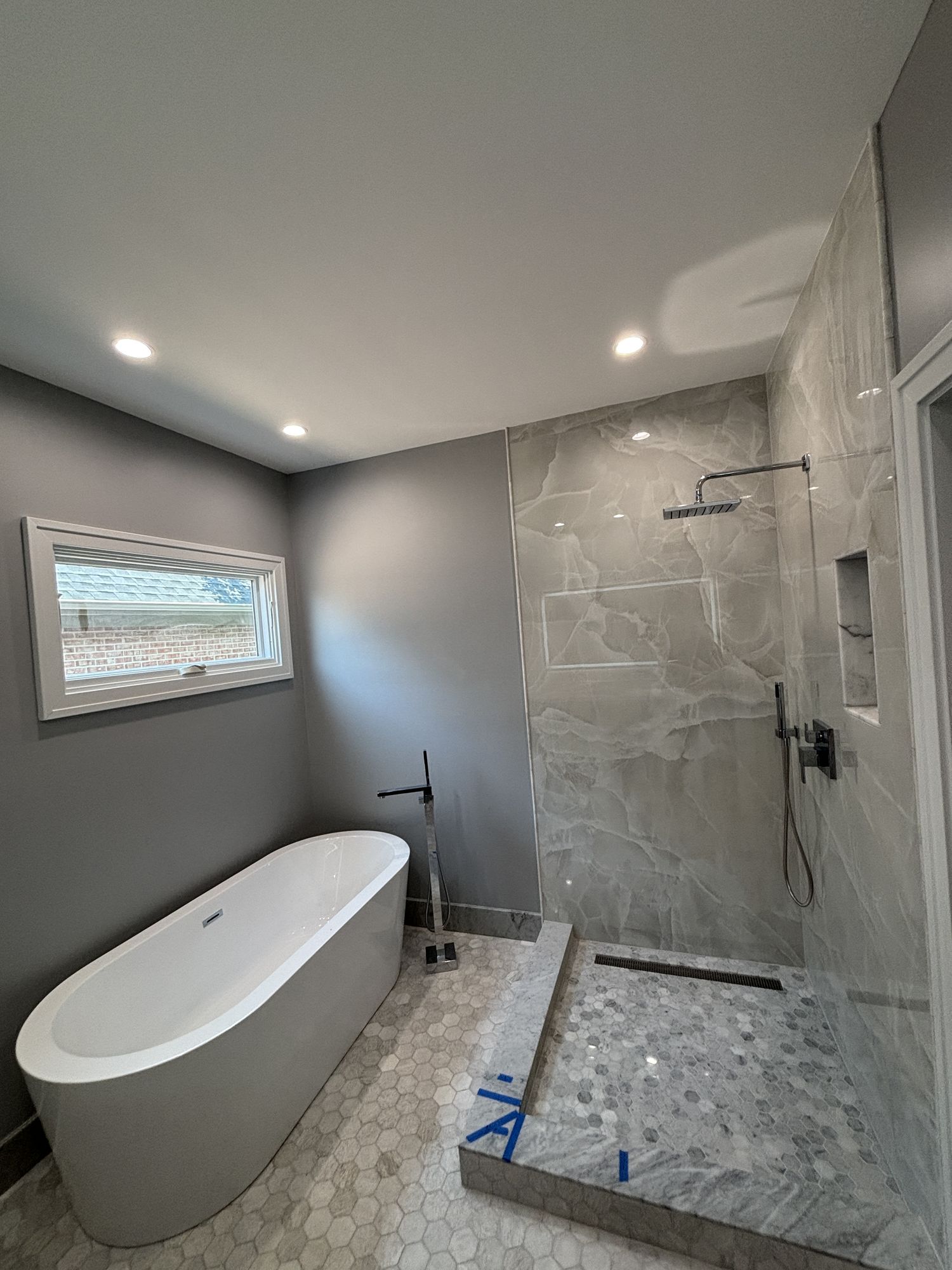 Bathroom under construction with a freestanding tub, onyx-look marble shower wall, and hexagon marble floor