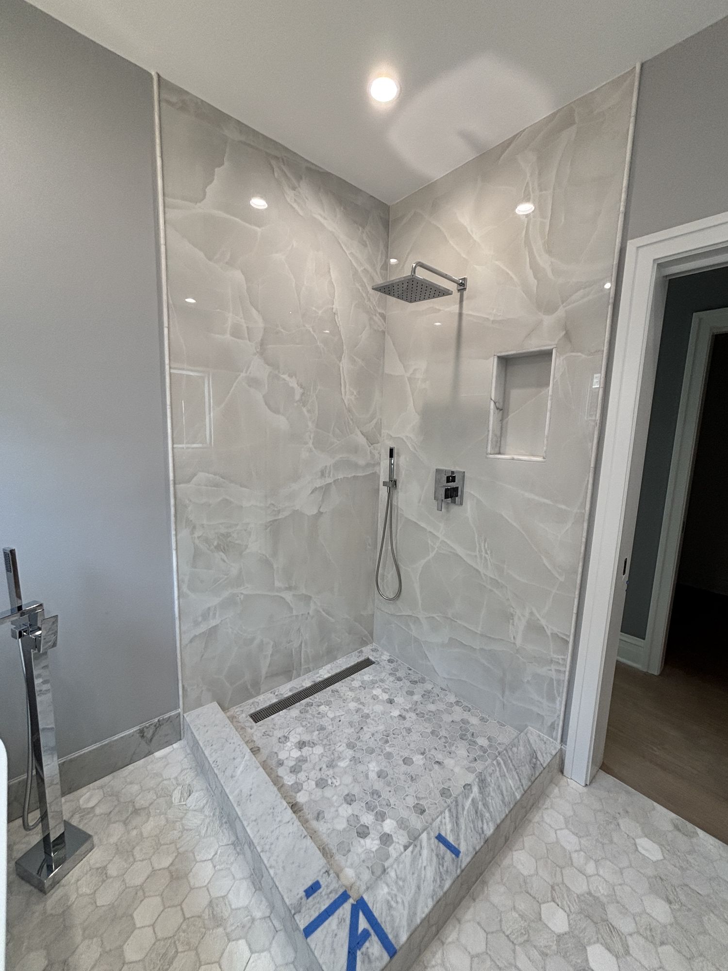 Onyx-look marble shower with a rain head and a built-in niche, mid-installation