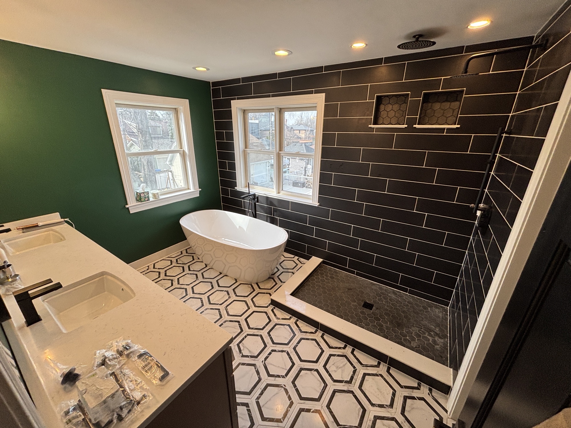 Remodeled primary bathroom with a freestanding tub, black tile shower wall, and hexagon marble floor